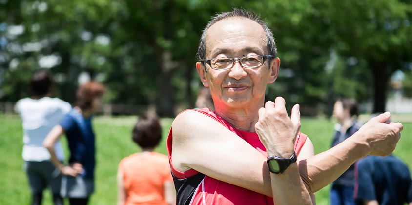 Elderly man with glasses in red singlet stretching for exercise