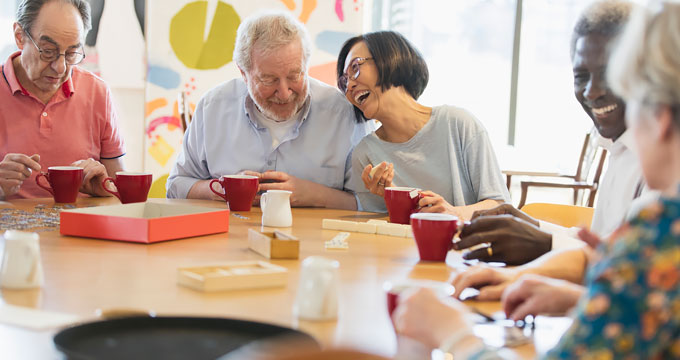 Group of retired men and women sitting at table laughing and playing card games